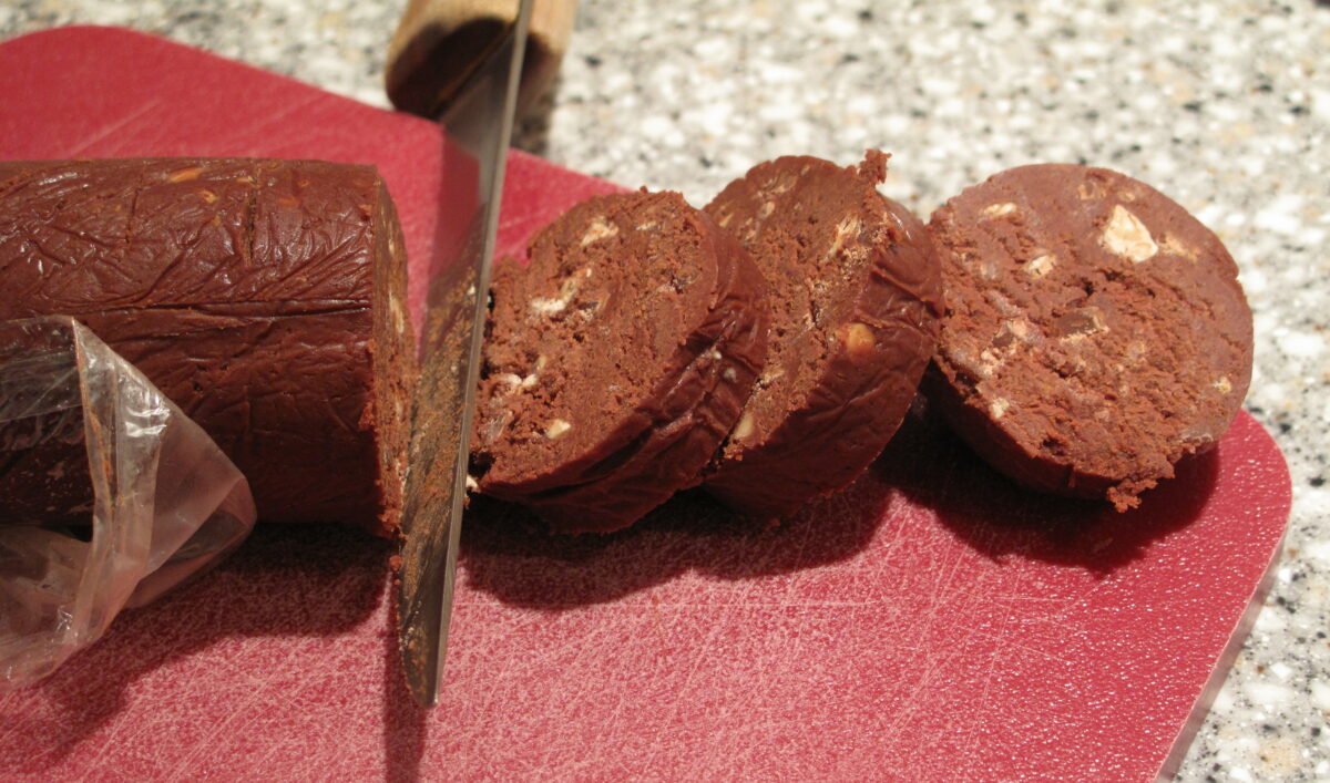 Dough log being sliced into cookies on a red cutting board.