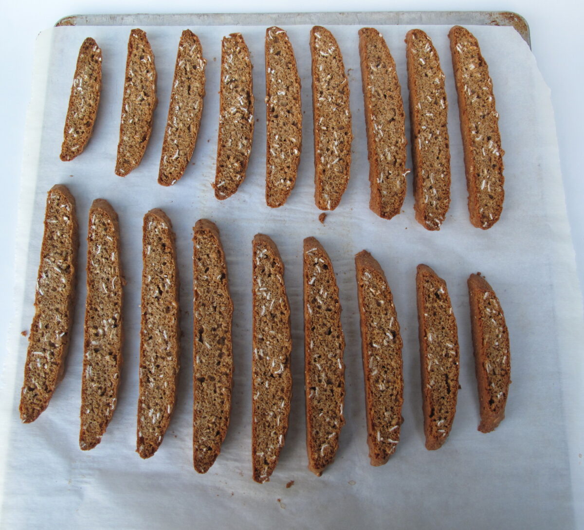 Sliced biscotti lying on cut edge on a parchment lined baking sheet.