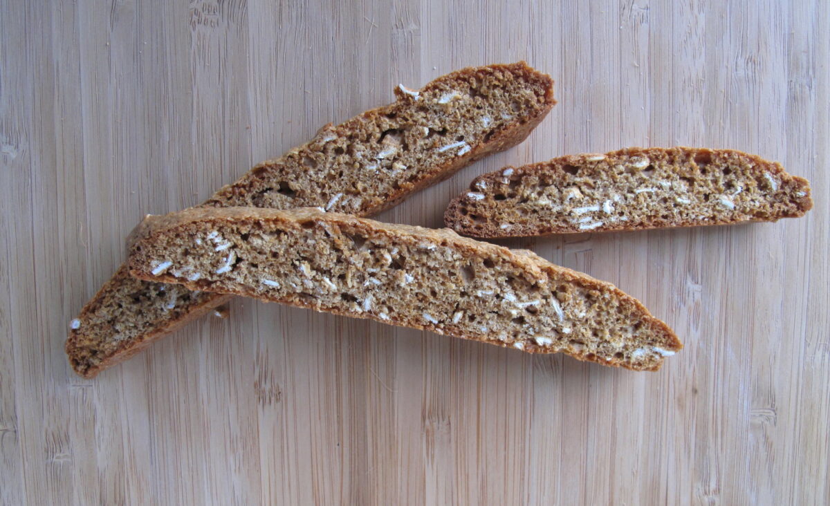 Three oat speckled biscotti on a wooden cutting board.