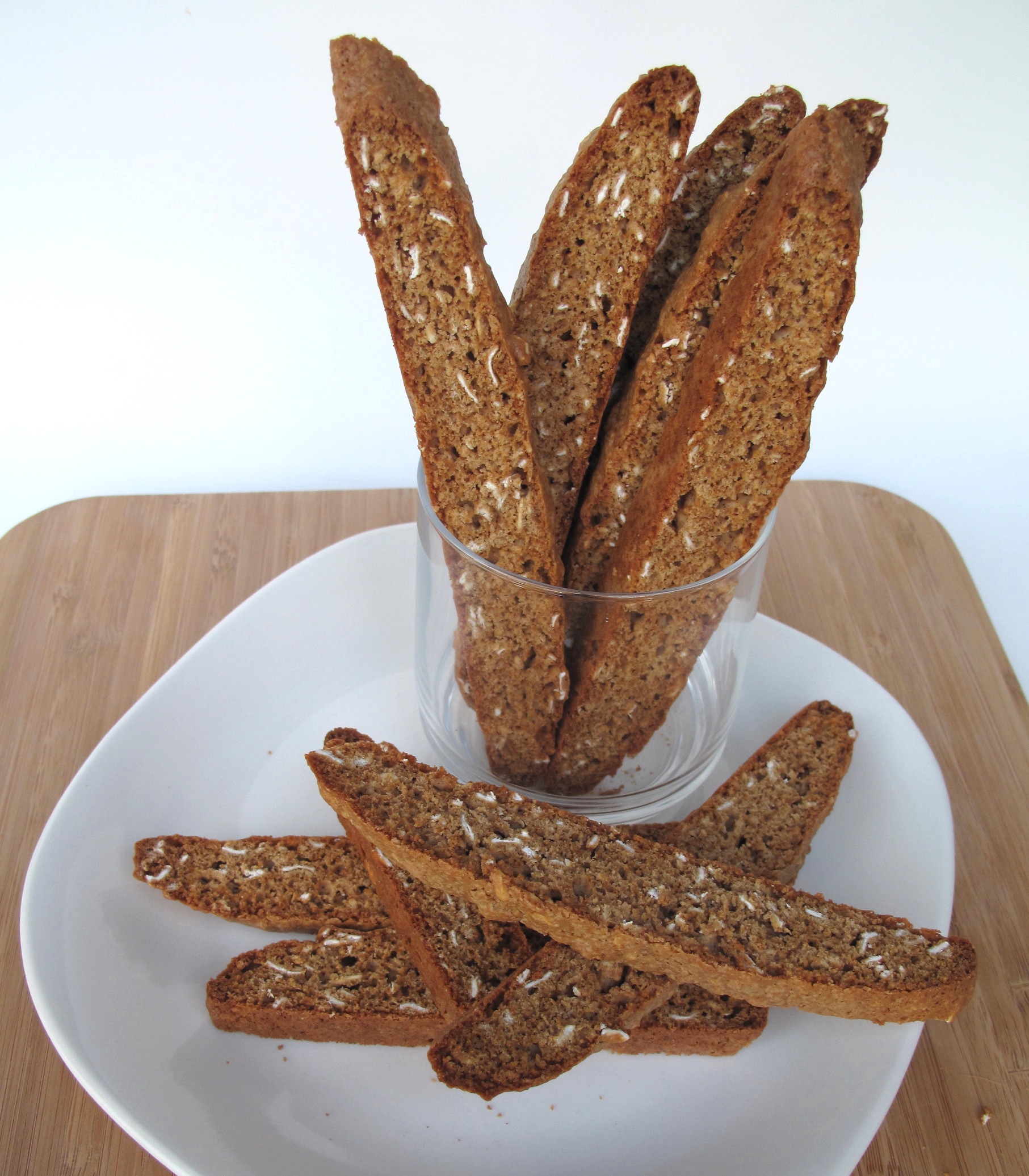 Cinnamon Maple Oat Biscotti standing in a glass and lying on a plate.