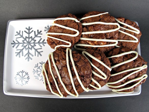 Cookies with white chocolate zigzags on top on a white serving tray.