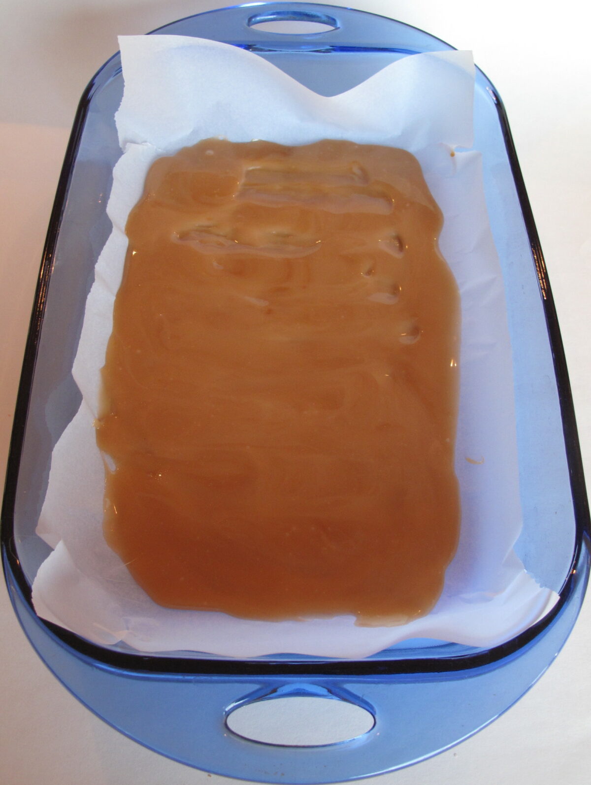 Homemade toffee firming in a blue glass baking dish lined with parchment.
