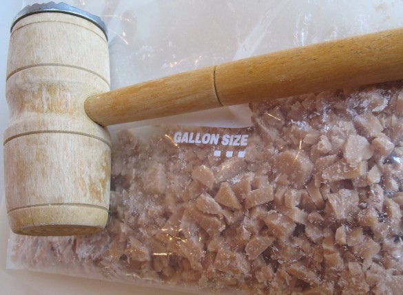 Toffee bits inside a plastic bag with a meat hammer.