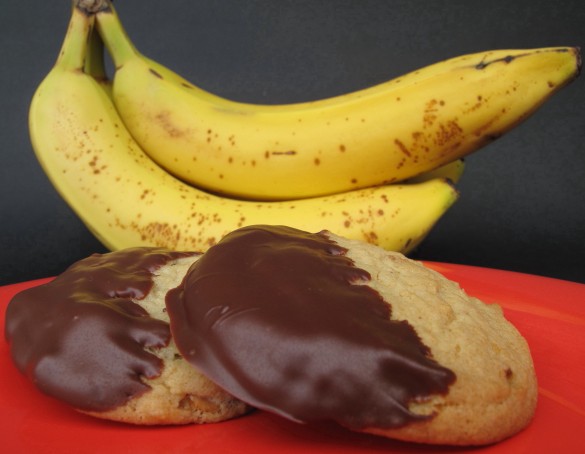 Two cookies on a red plate with bananas in the background.