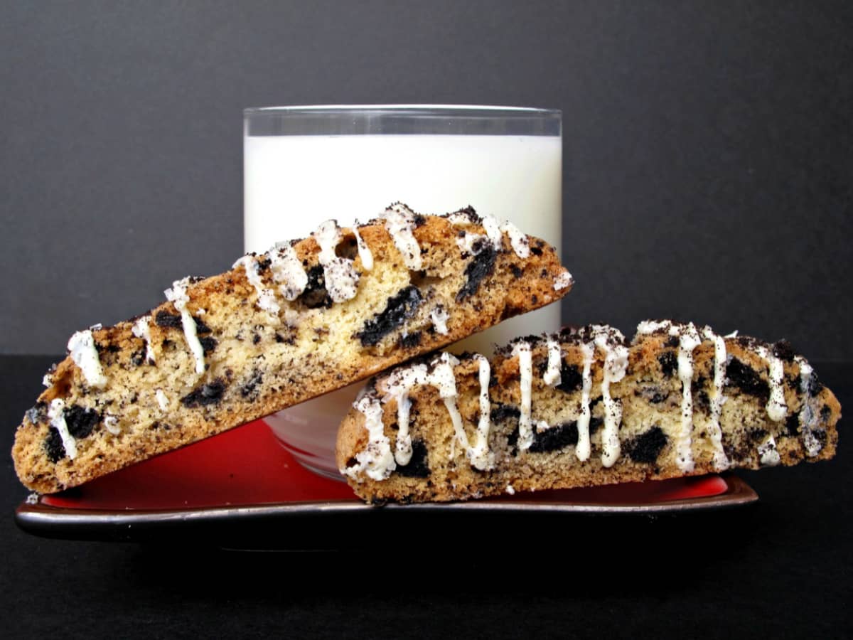 Two biscotti with chocolate cookie bits inside on a red plate with a glass of milk.
