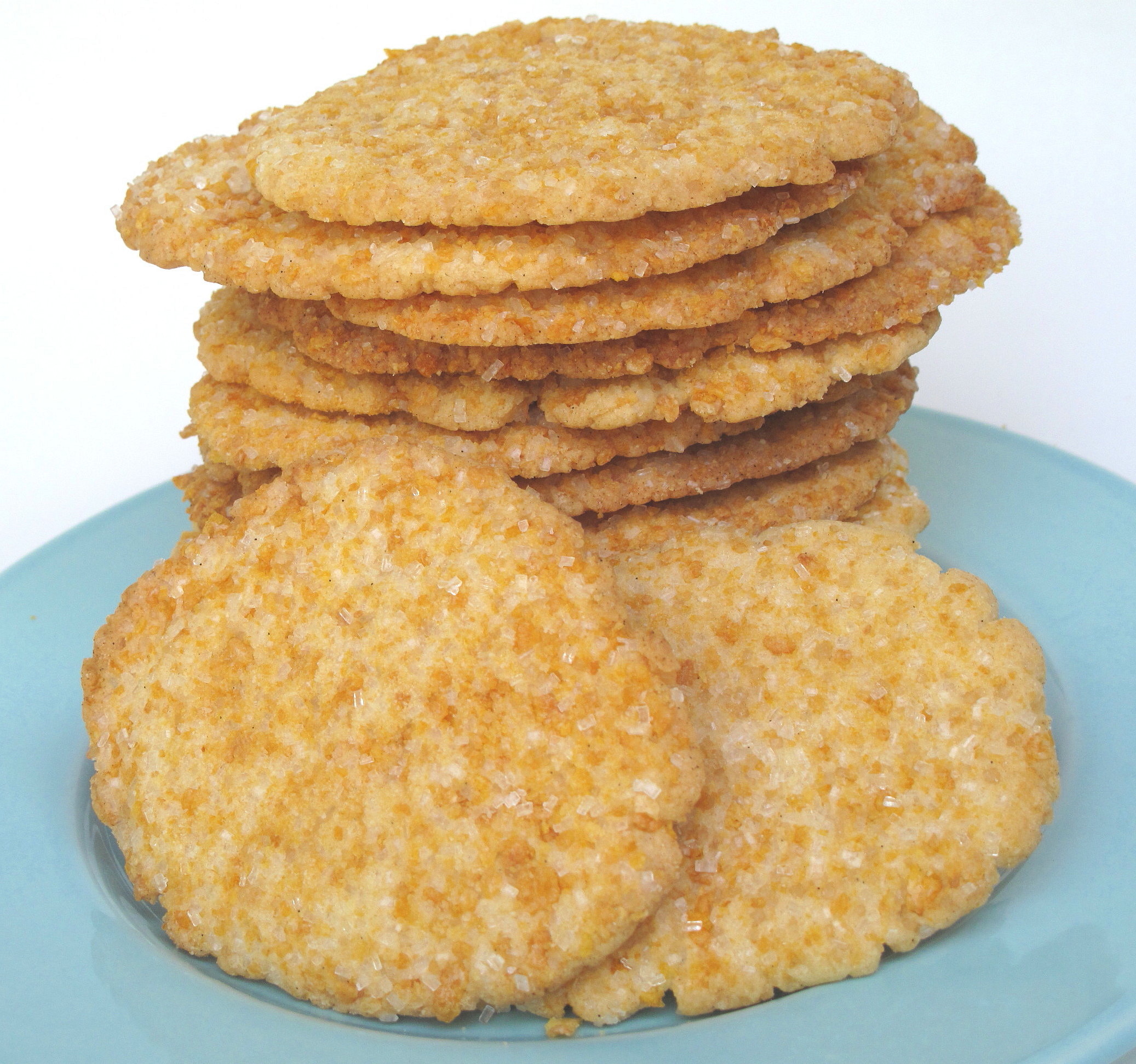 Thin sugar cookies coated in crushed frosted flakes and sugar, stacked on a blue plate.