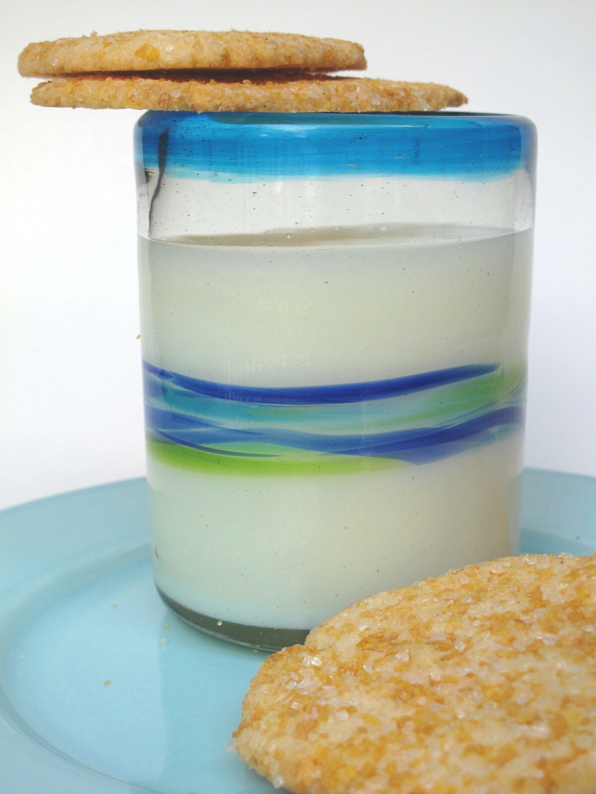 Two thin cookies balanced on the rim of a glass of milk.