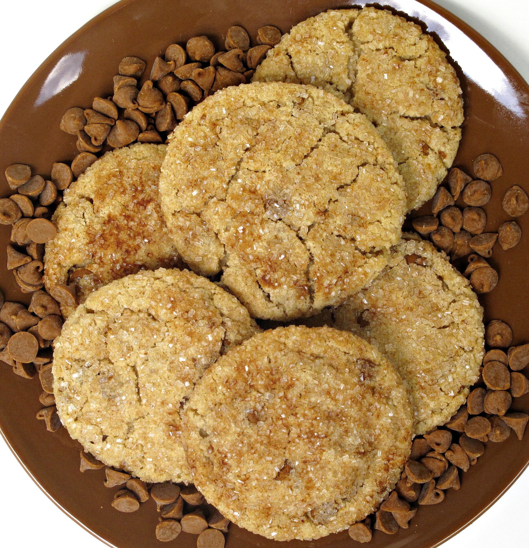 Cookies with a crackled surface coated in sparkling sugar on a plate with cinnamon baking chips.