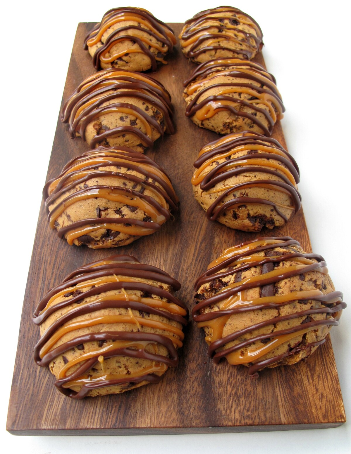 Wooden cutting board with two rows of rounded cookies decorated with chocolate and caramel zigzags.