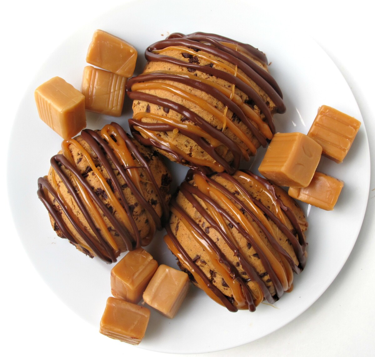 Overhead three cookies on a white plate with candy caramel squares.