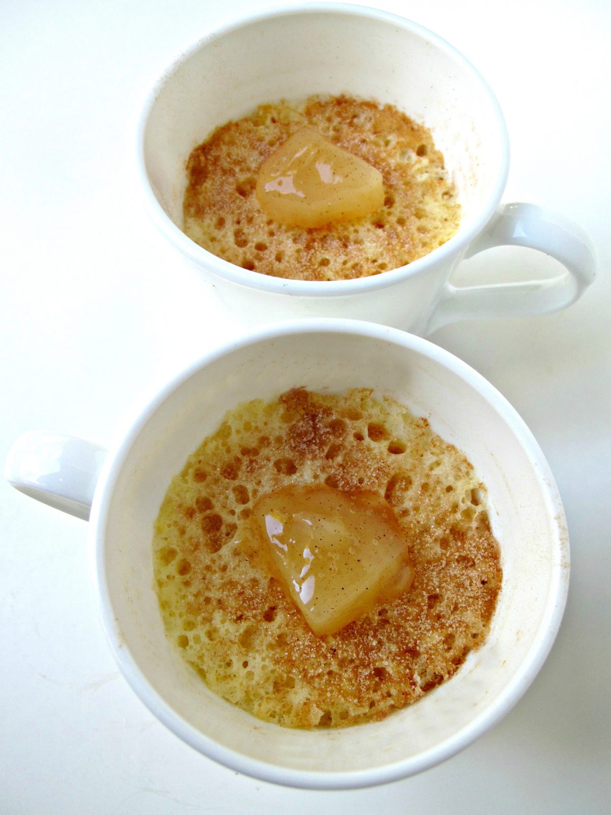 Two white mugs filled with cake and topped with a slice of apple. 