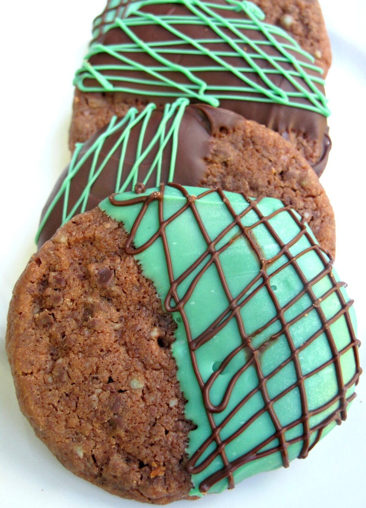 Closeup of a chocolate cookie dipped in melted green mint chips and drizzled with chocolate.