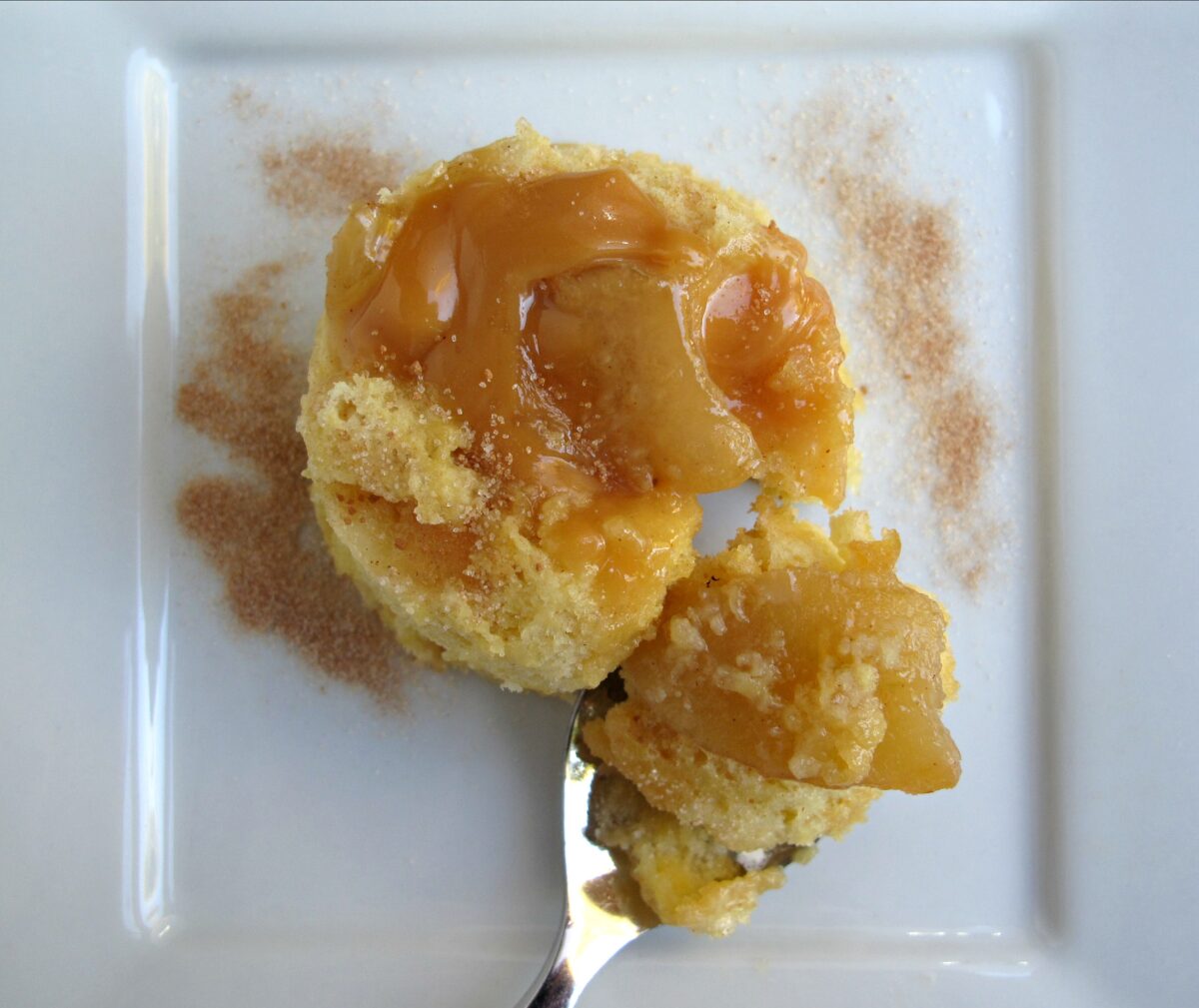 Overhead view of a Mug Cake on a plate topped with gooey caramel and apple slices.