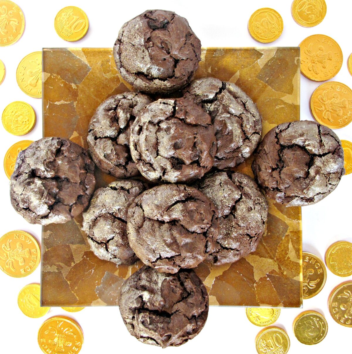 Chocolate cookies with gold dusted tops on a square gold plate with gold foil coins.