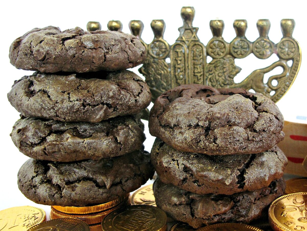 Two stacks of thick, chocolate cookies in front of a small  brass menorah.