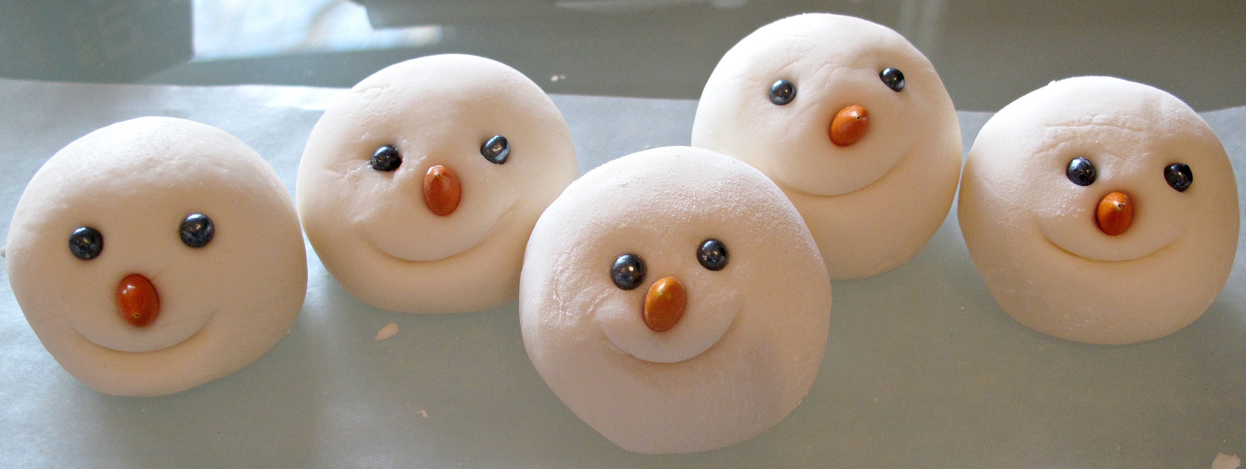 Closeup of 5 fondant heads with eyes, noses, and indented smile mouths.