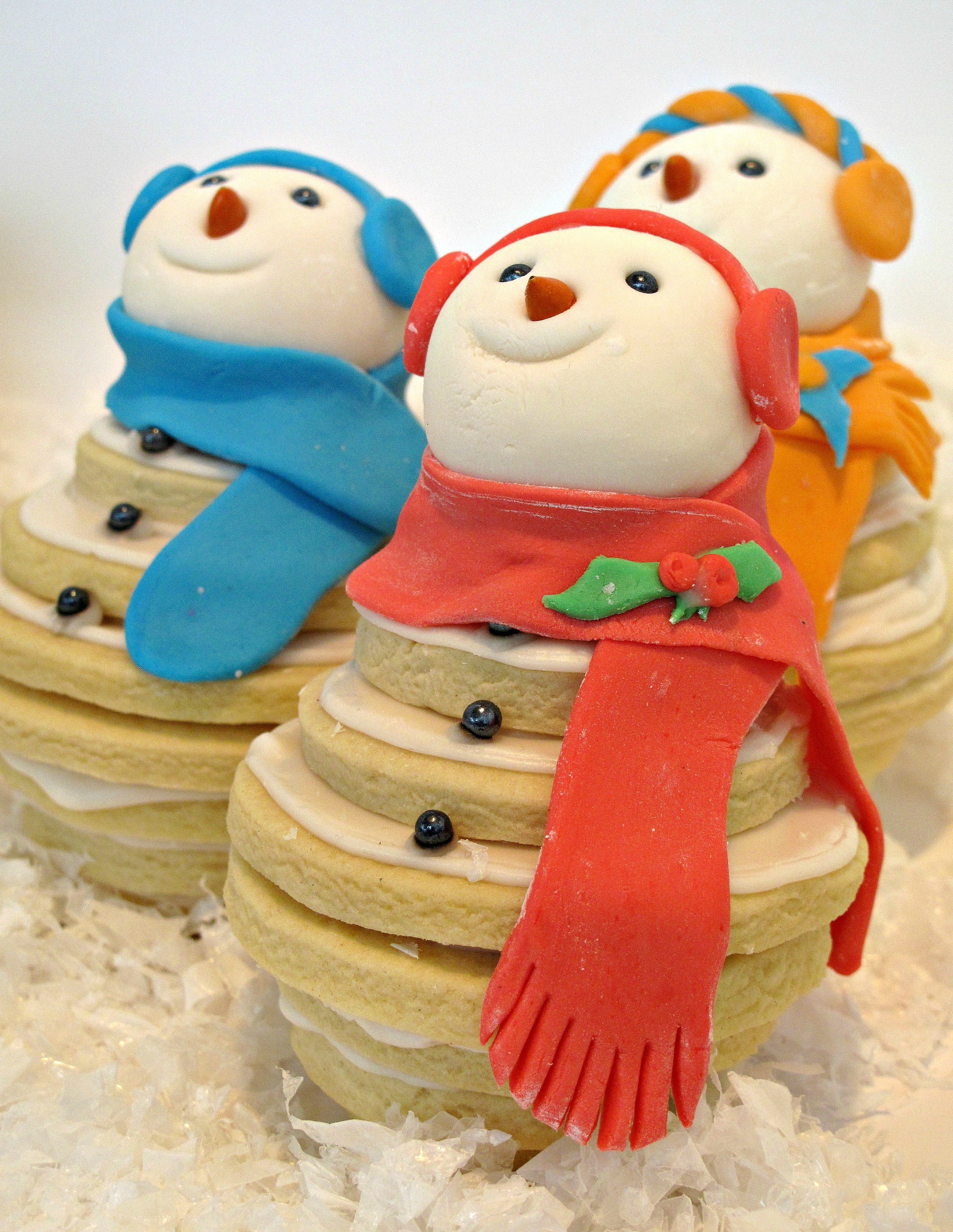 Closeup of a snowman cookie wearing a red scarf and red ear muffs.