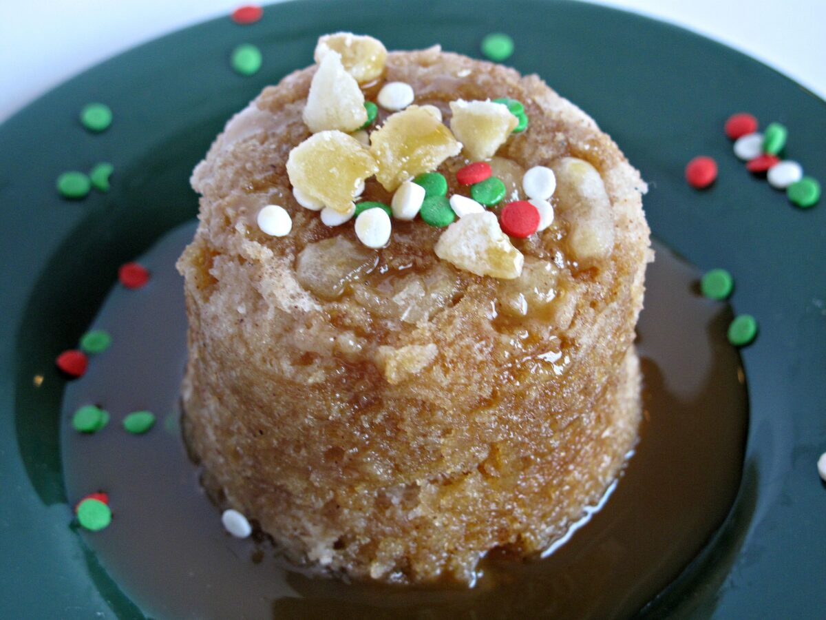 Gingerbread Mug Cake with caramel syrup on a green plate surrounded by caramel syrup and red and green sprinkles.