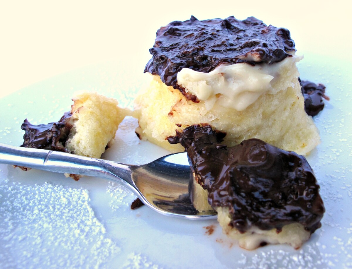 Spoonful of chocolate covered Boston Cream Pie Mug Cake with the cake in the background.