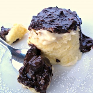 Boston Cream Pie Mug Cake on a plate behind a spoon full of cake covered in melted chocolate.