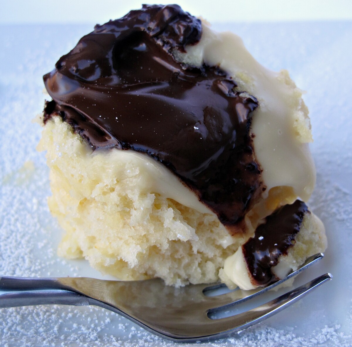 Boston Cream Pie Mug Cake topped with melted chocolate and vanilla pudding with a fork.