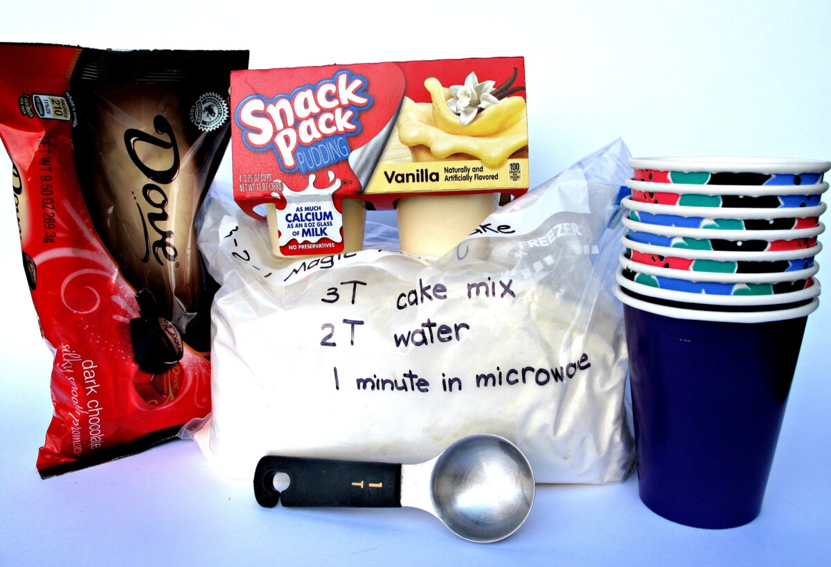 Ingredients for Boston Cream Pie Mug Cake including cake mix, pudding, chocolate candy, tablespoon, paper cups.