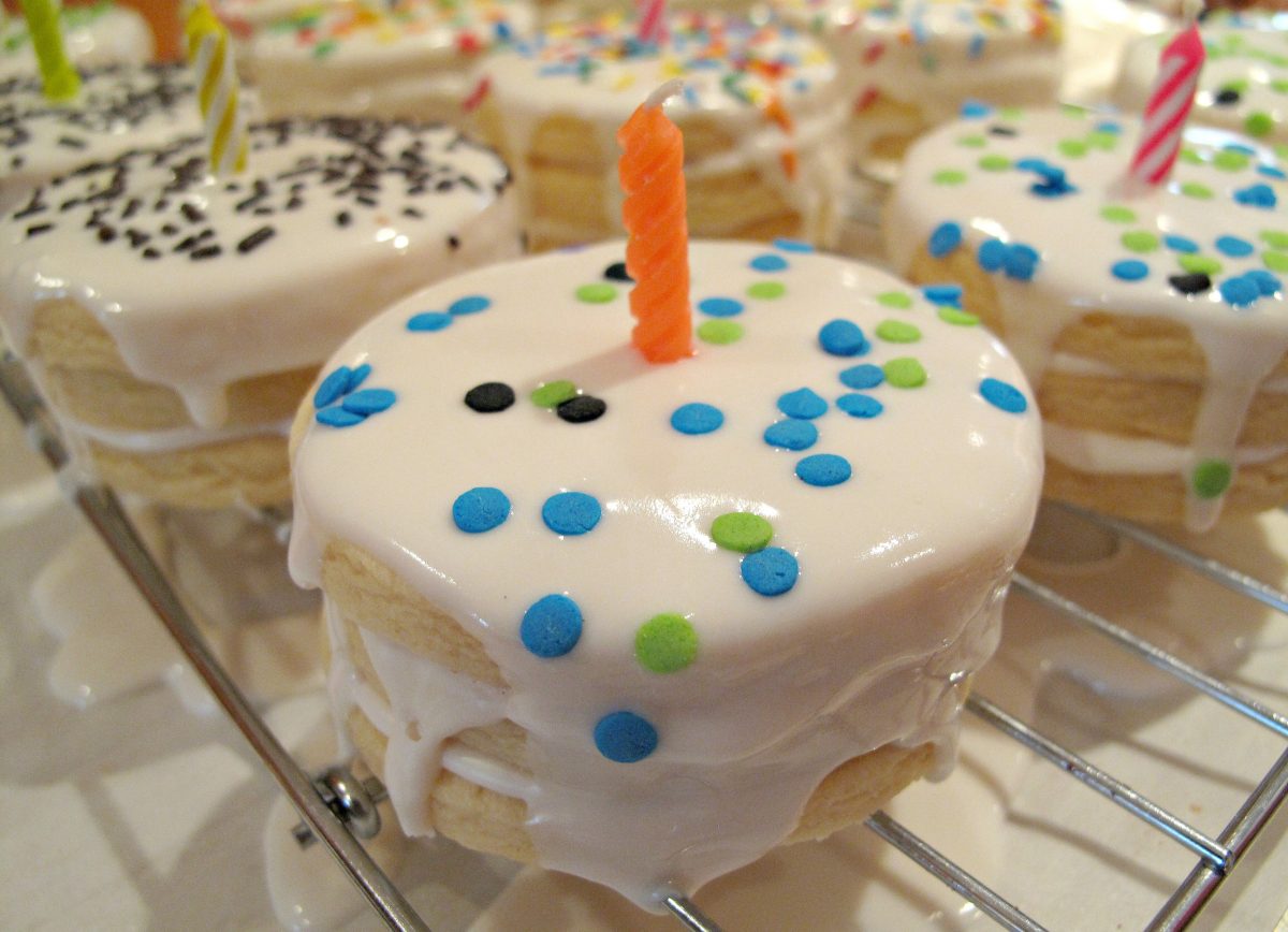 Birthday Cake Surprise Cookies made of vanilla sugar cookies, topped with white glaze, sprinkles, candle.