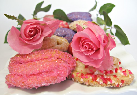 Rose Bud Butter Cookies, one coated in pink sugar and another coated in heart sprinkles and two pink roses