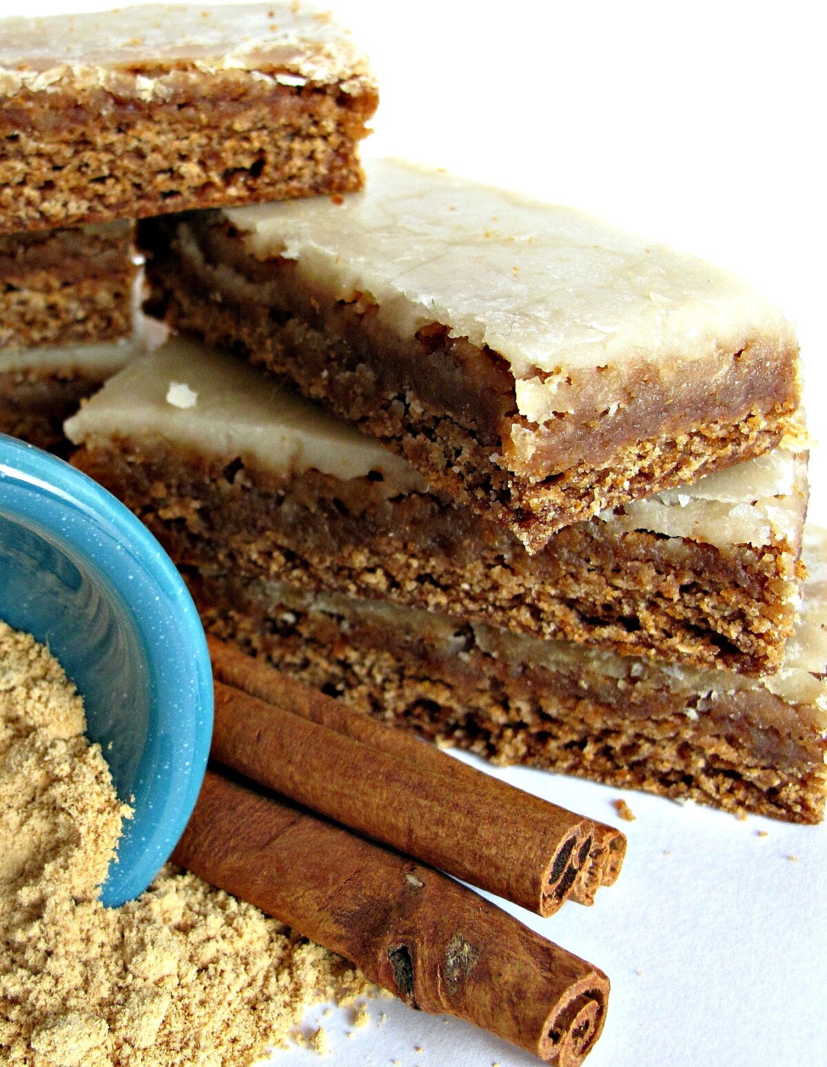  Lebkuchen Bars with Orange-Ginger Glaze stacked next to cinnamon sticks and ginger powder.