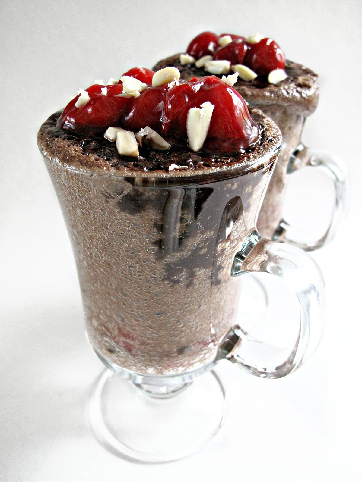 Chocolate cake in a mug topped with cherries and almonds.
