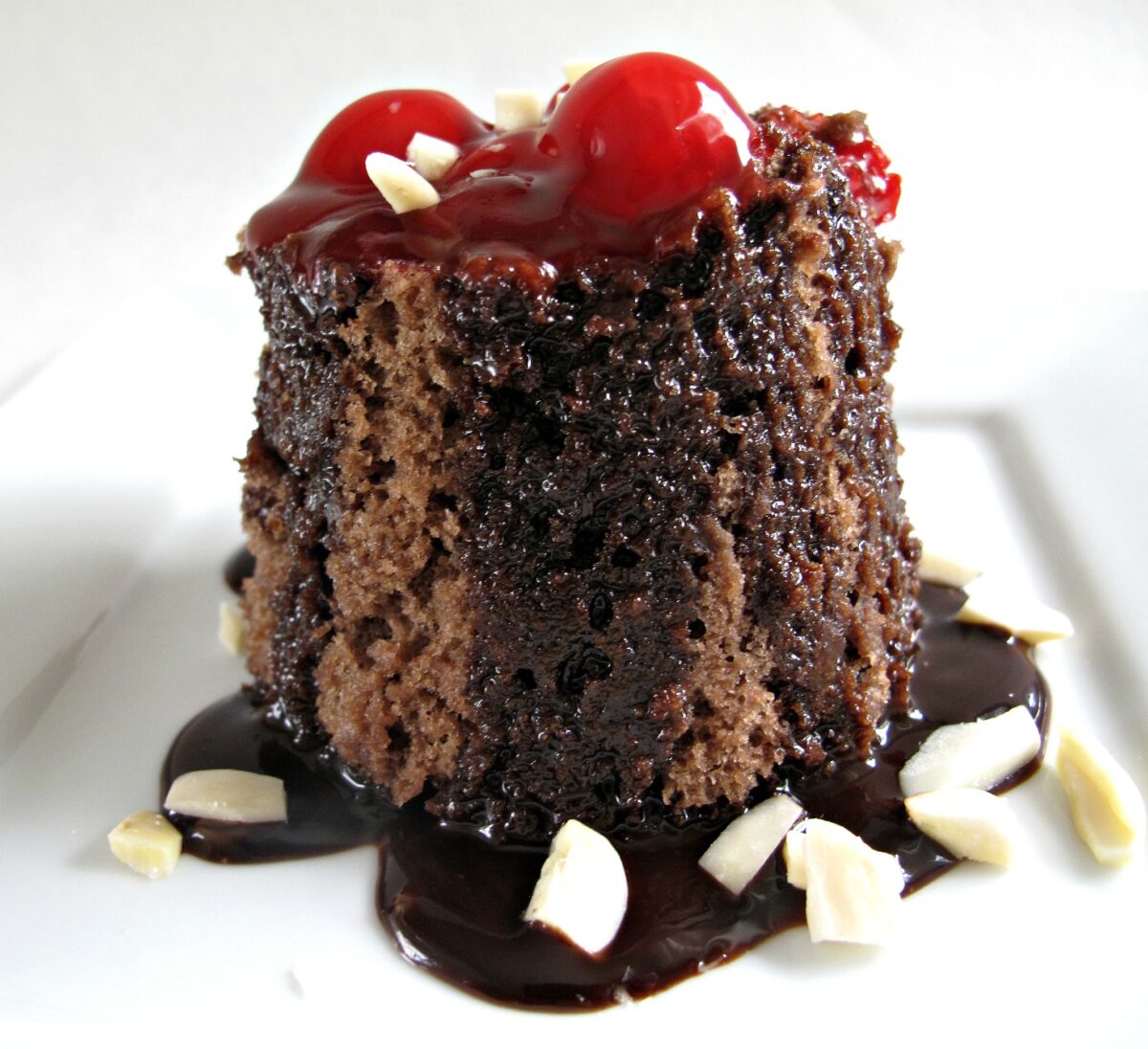 Chocolate mug cake on a plate topped with cherry pie filling, chocolate sauce, and almonds.