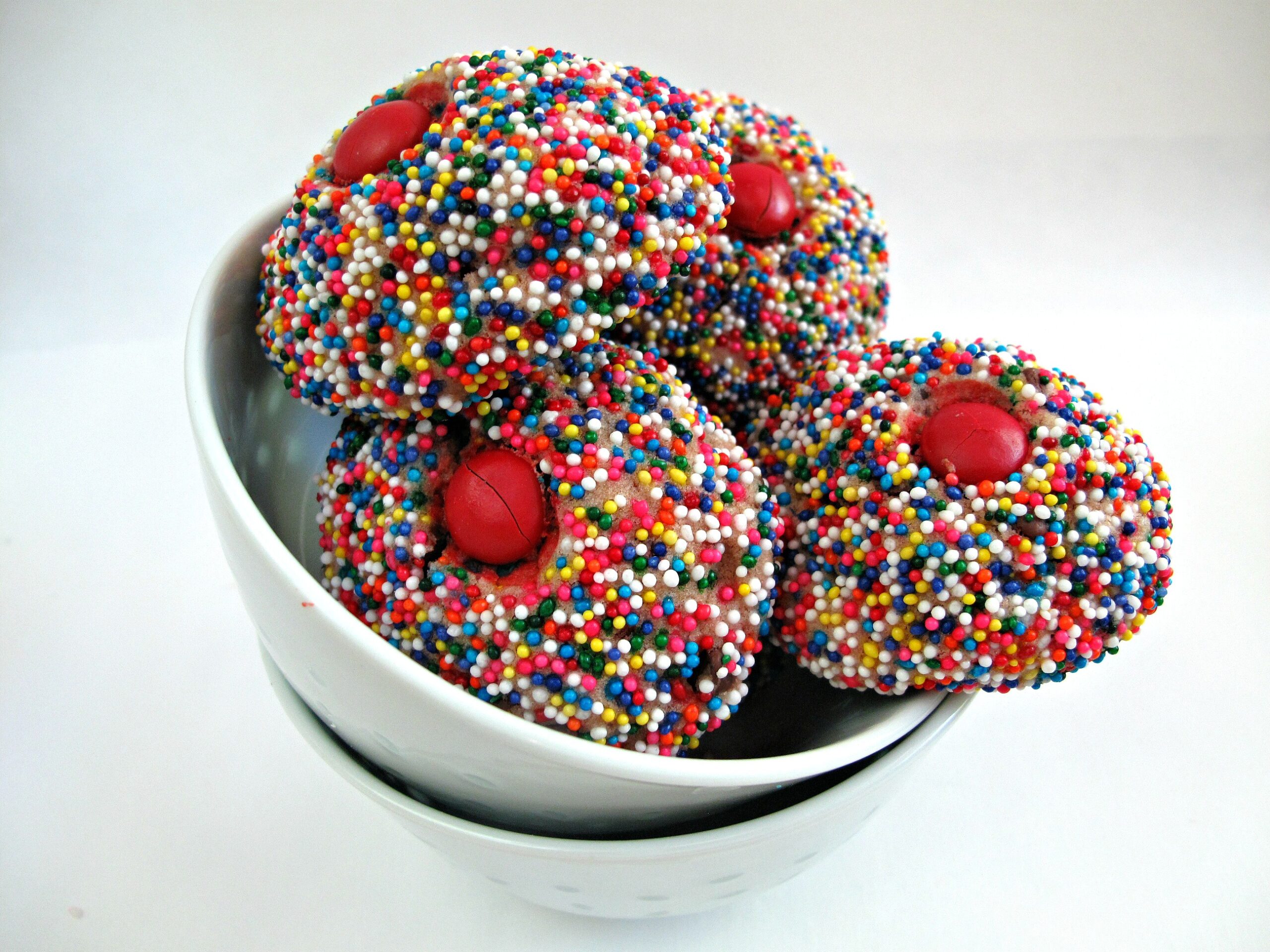 Round cookies covered in multicolored nonpareils and a red candy on top like icecream scoops.