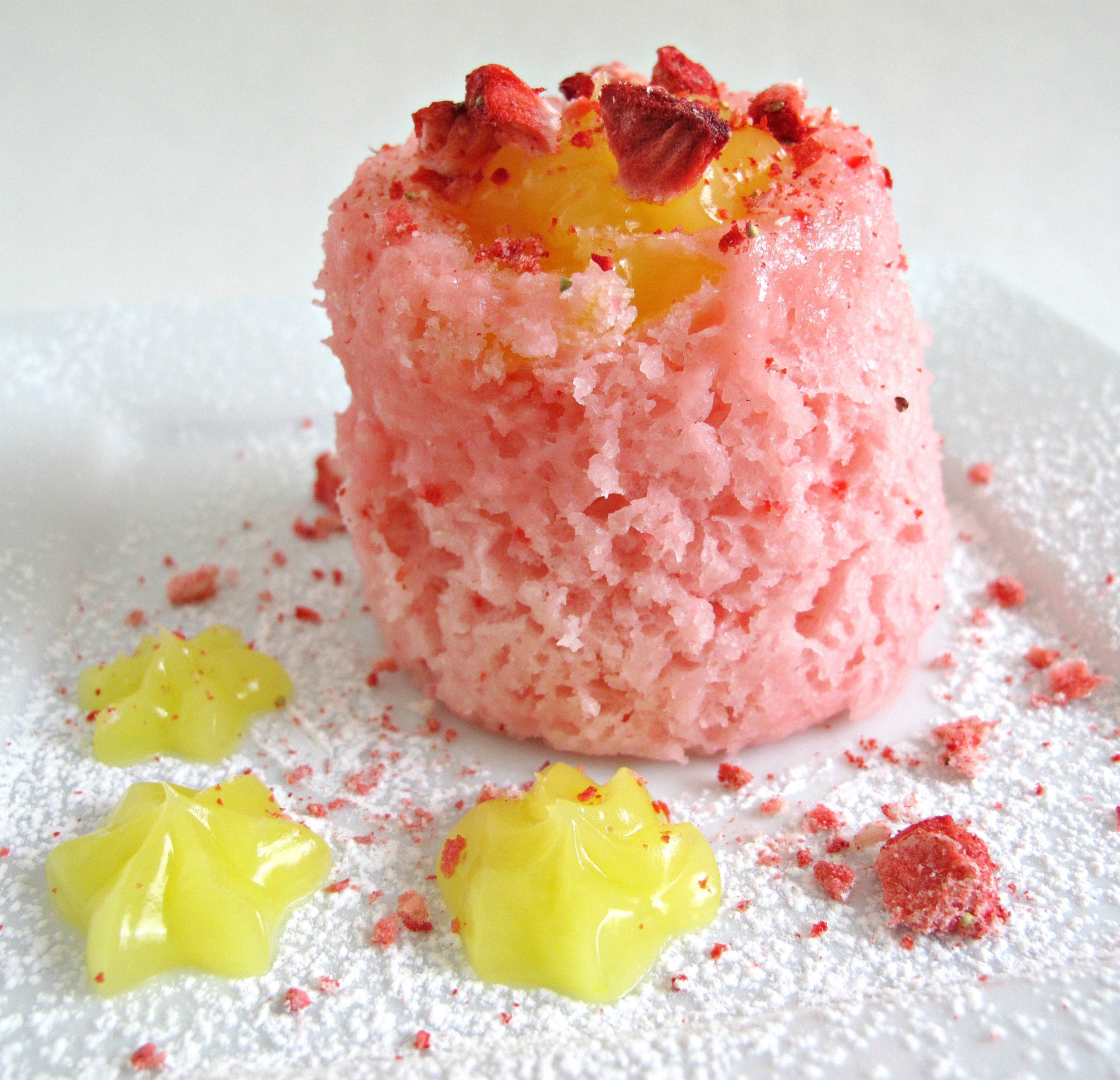 Fluffy, pink cake on a plate sprinkled with powdered sugar, freeze dried strawberries, and lemon curd.
