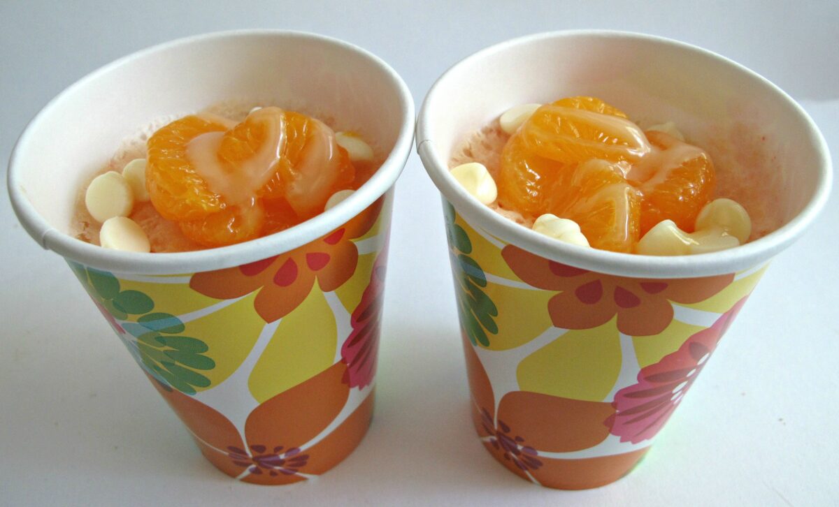 Two Mandarin Orange  Mug Cakes in paper cups topped with oranges and white chocolate chips.