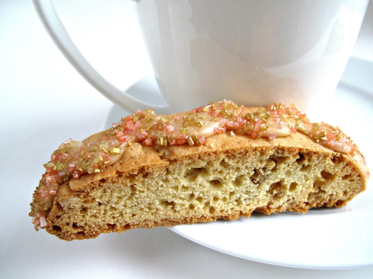 Biscotti on the edge of a white saucer next to a white mug.