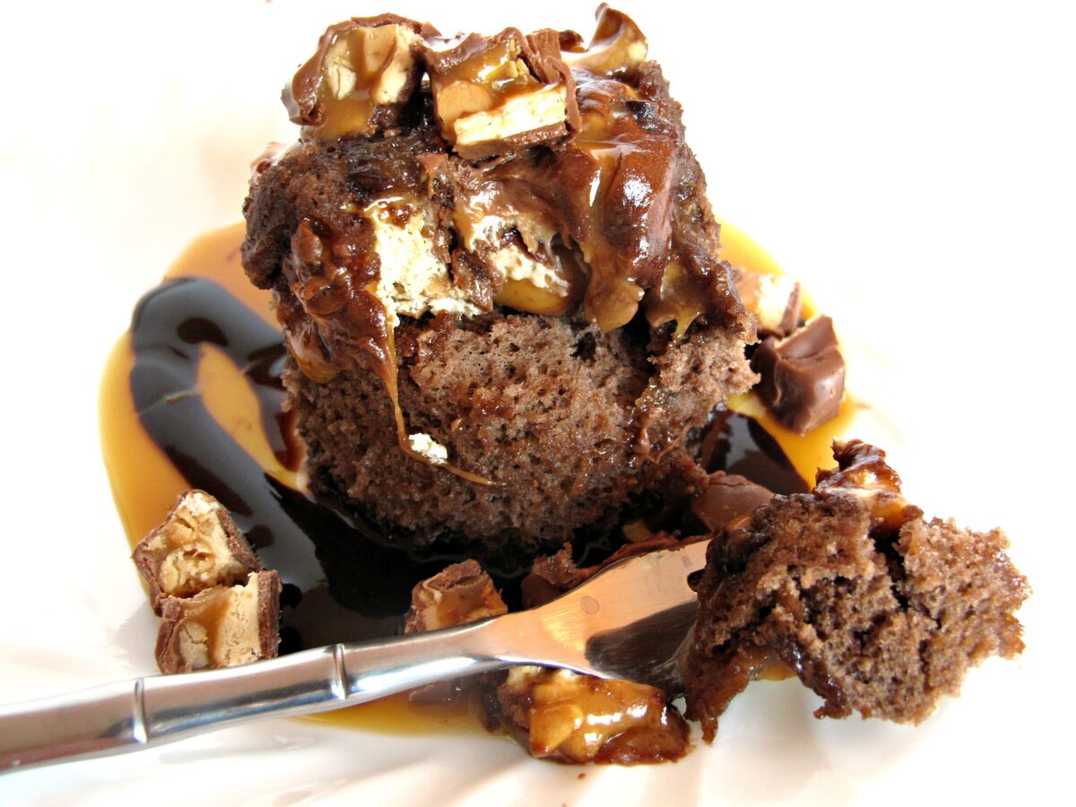 Chocolate mug cake on a plate topped with melted candy bar pieces.