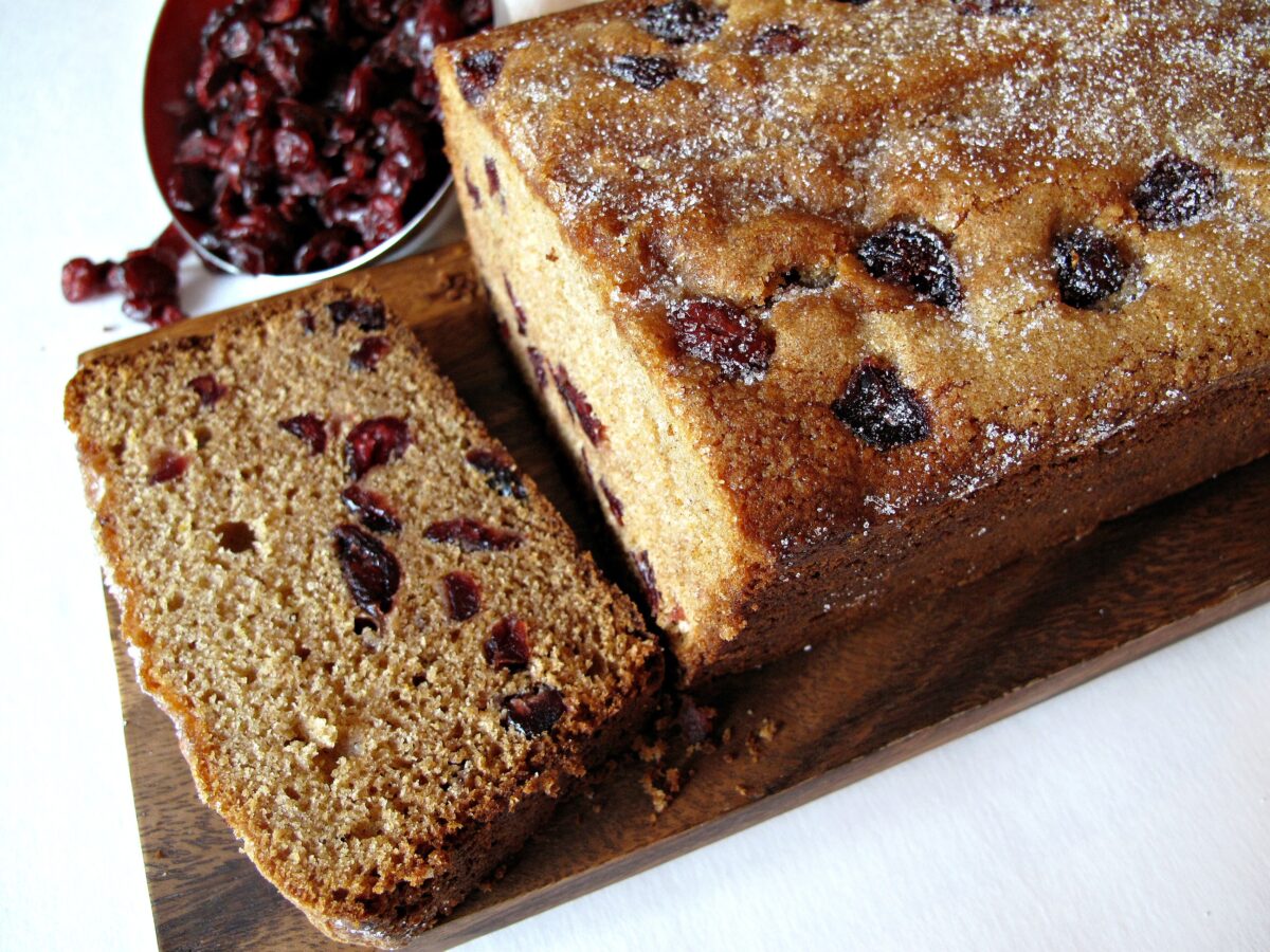 A loaf of Cranberry Clementine Whole Wheat Quick Bread with one piece sliced.