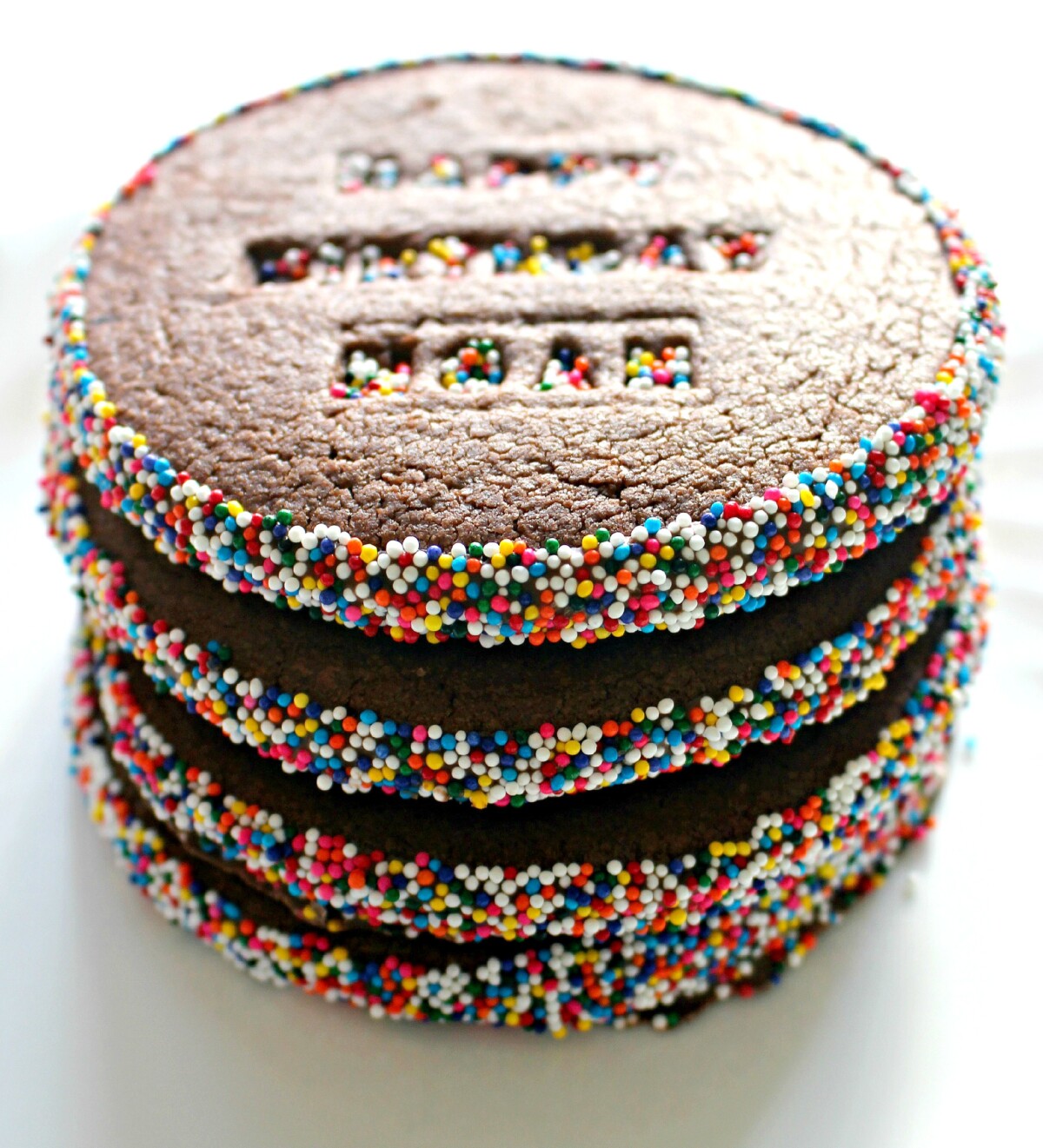 Stack of chocolate cookies with multicolored nonpareil sprinkles on their edges.