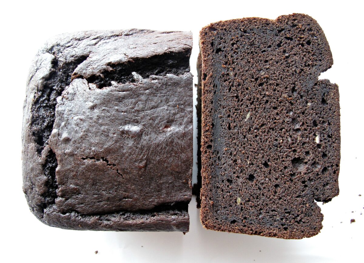Stack of slices showing dense chocolate crumb next to shiny topped half loaf .