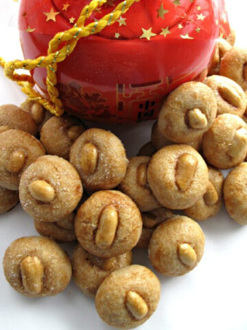Small, peanut topped cookies in front of a red cookie jar.