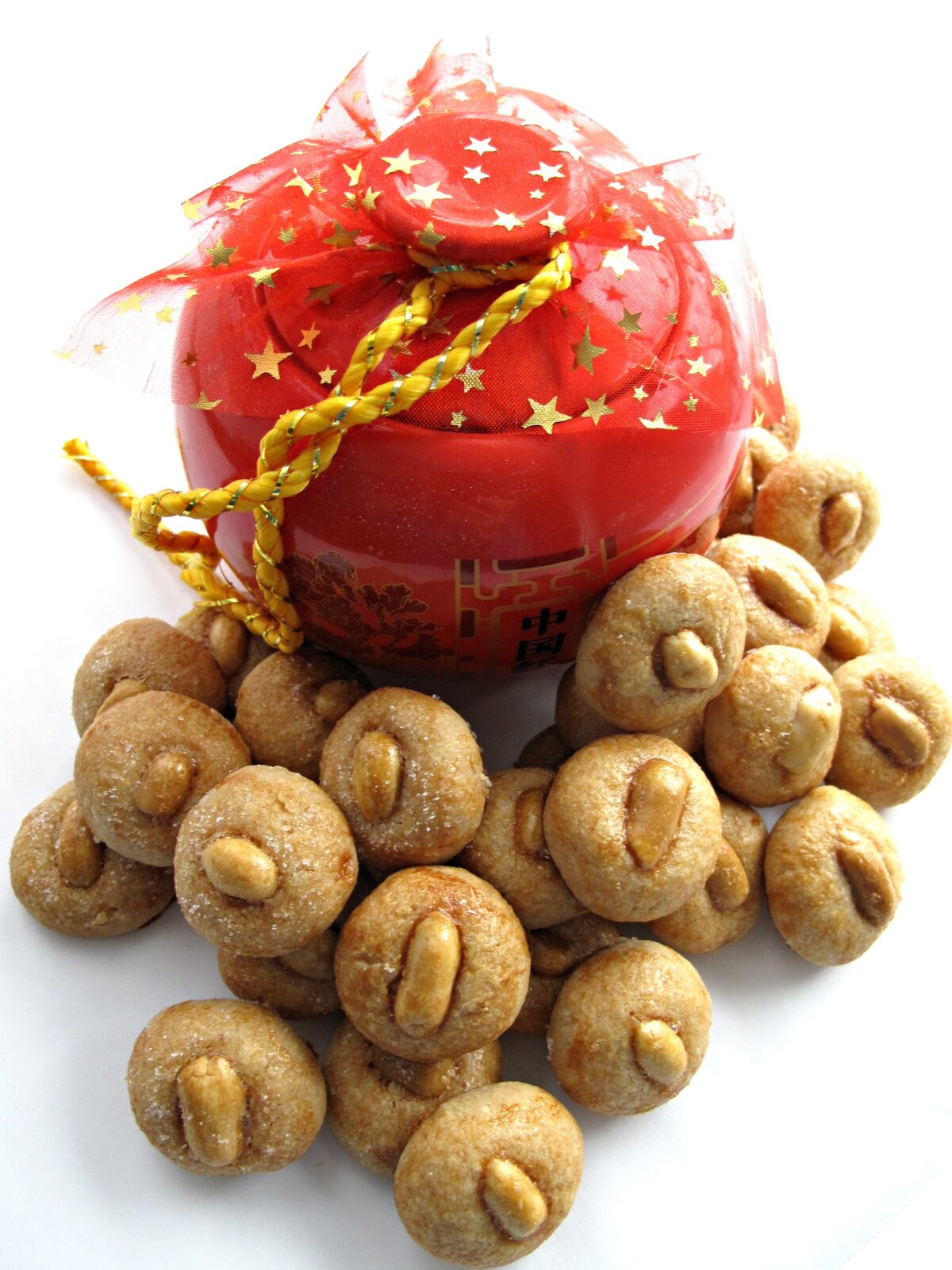 Ball shaped, little cookies topped with a peanut, in front of a red Chinese cookie jar.
