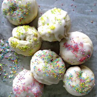 Ball shaped cookies with white icing and pastel nonpareil sprinkles.
