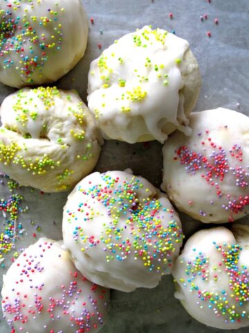 Ball shaped cookies with white icing and pastel nonpareil sprinkles.