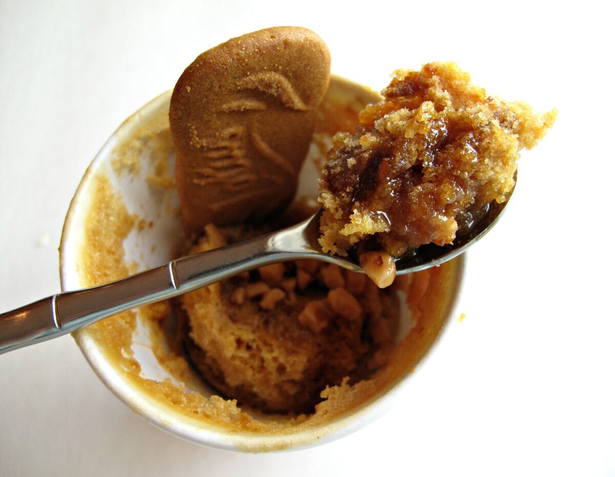 Biscoff  Mug Cake in a cup with a spoon and a biscoff cookie.