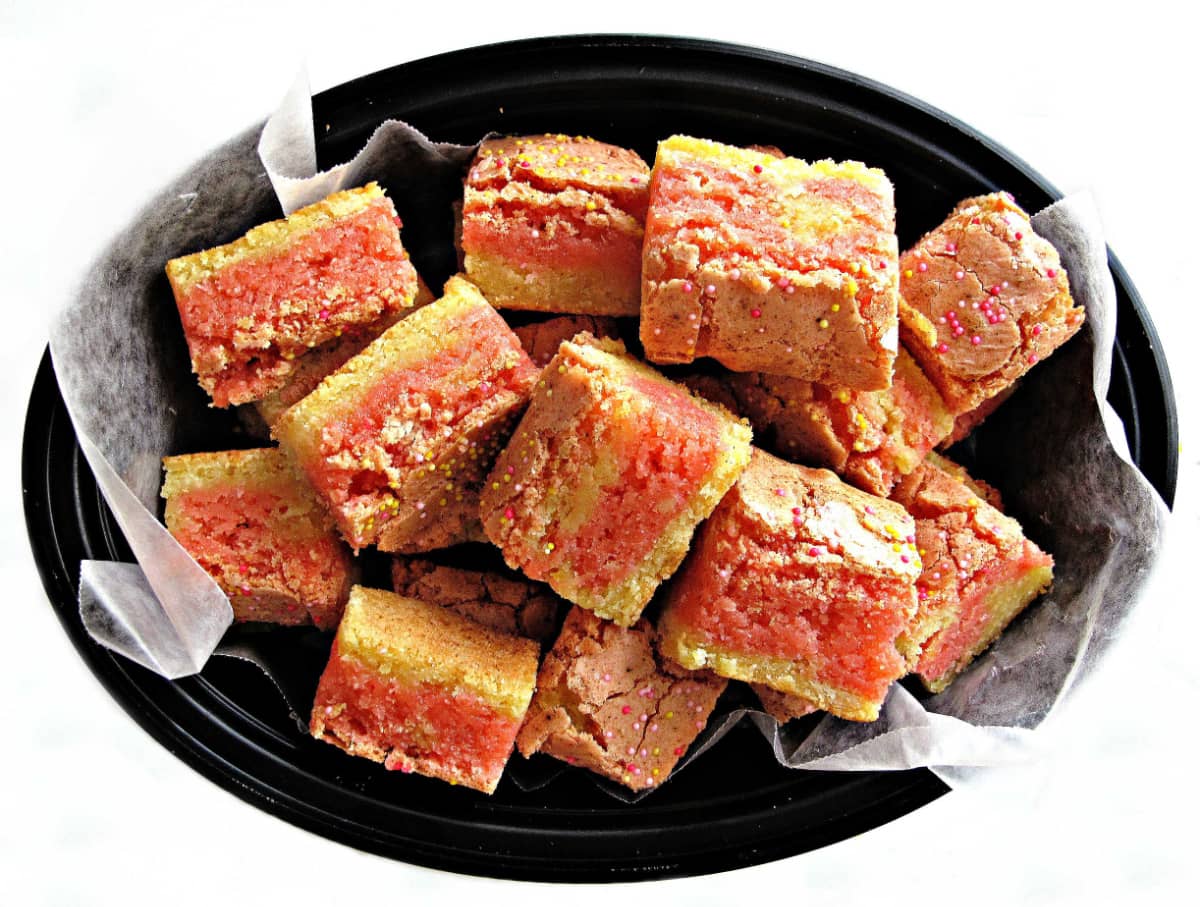 Pink and yellow striped, thick and chewy Strawberry Lemon Bars in a black bowl.