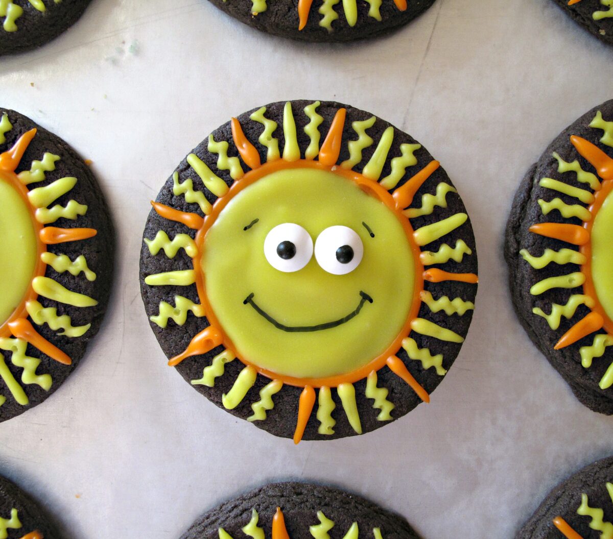 Closeup of chocolate sugar cookie circle decorated like a smiling face sun with candy sprinkle eyes.