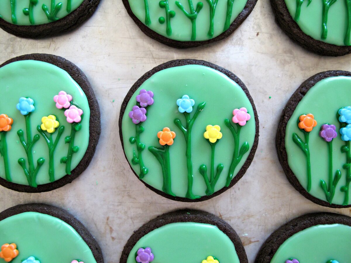 Closeup of chocolate sugar cookie circles iced green with green stems and sprinkle flowers.