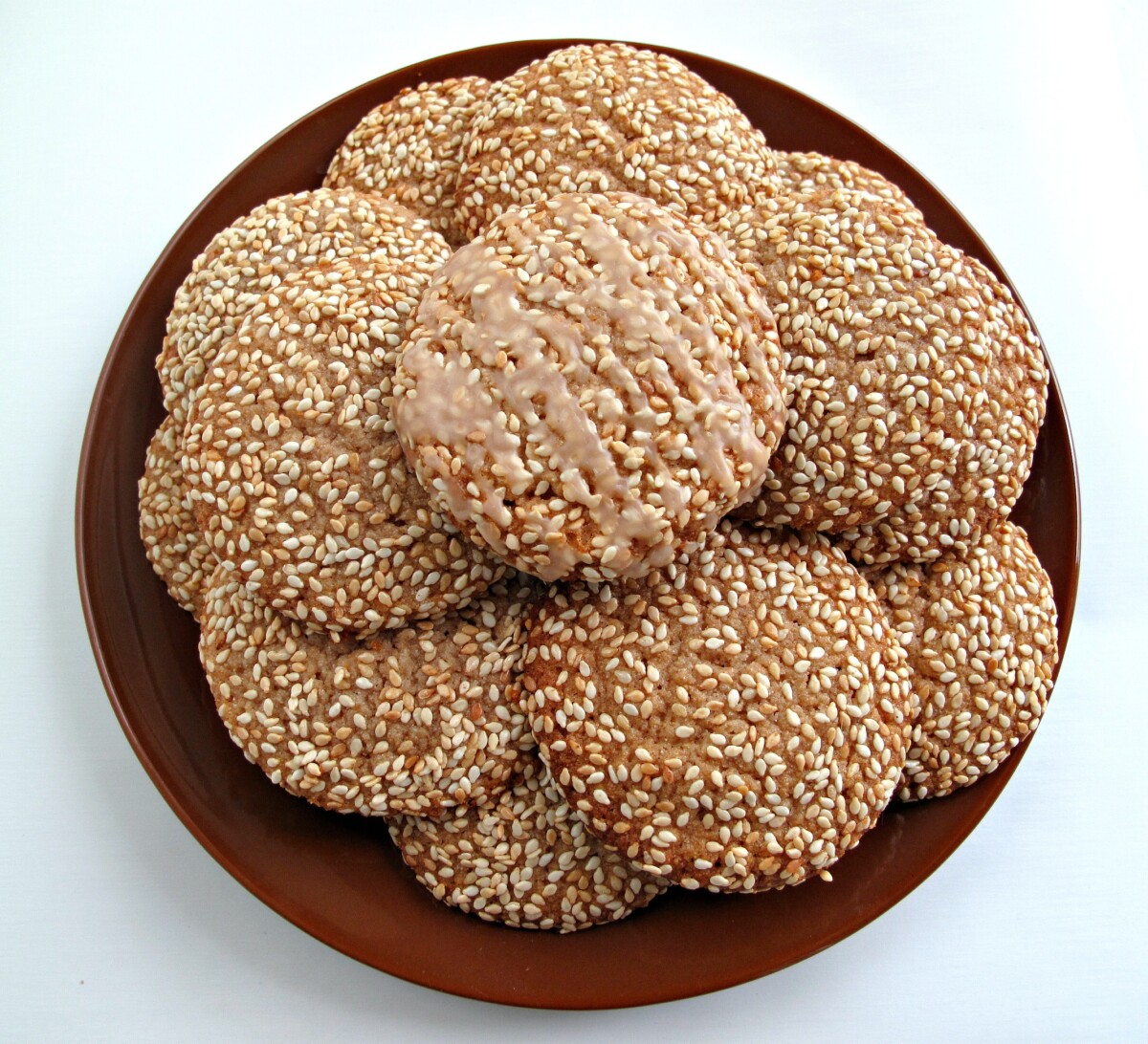 Sesame seed covered cookies on a brown serving plate.