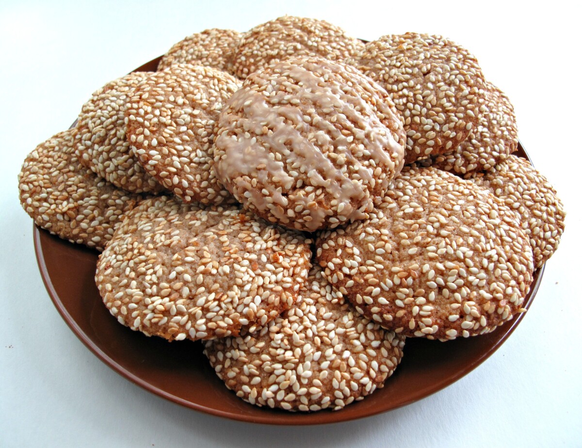 Sesame seed covered cookies on a brown serving plate.