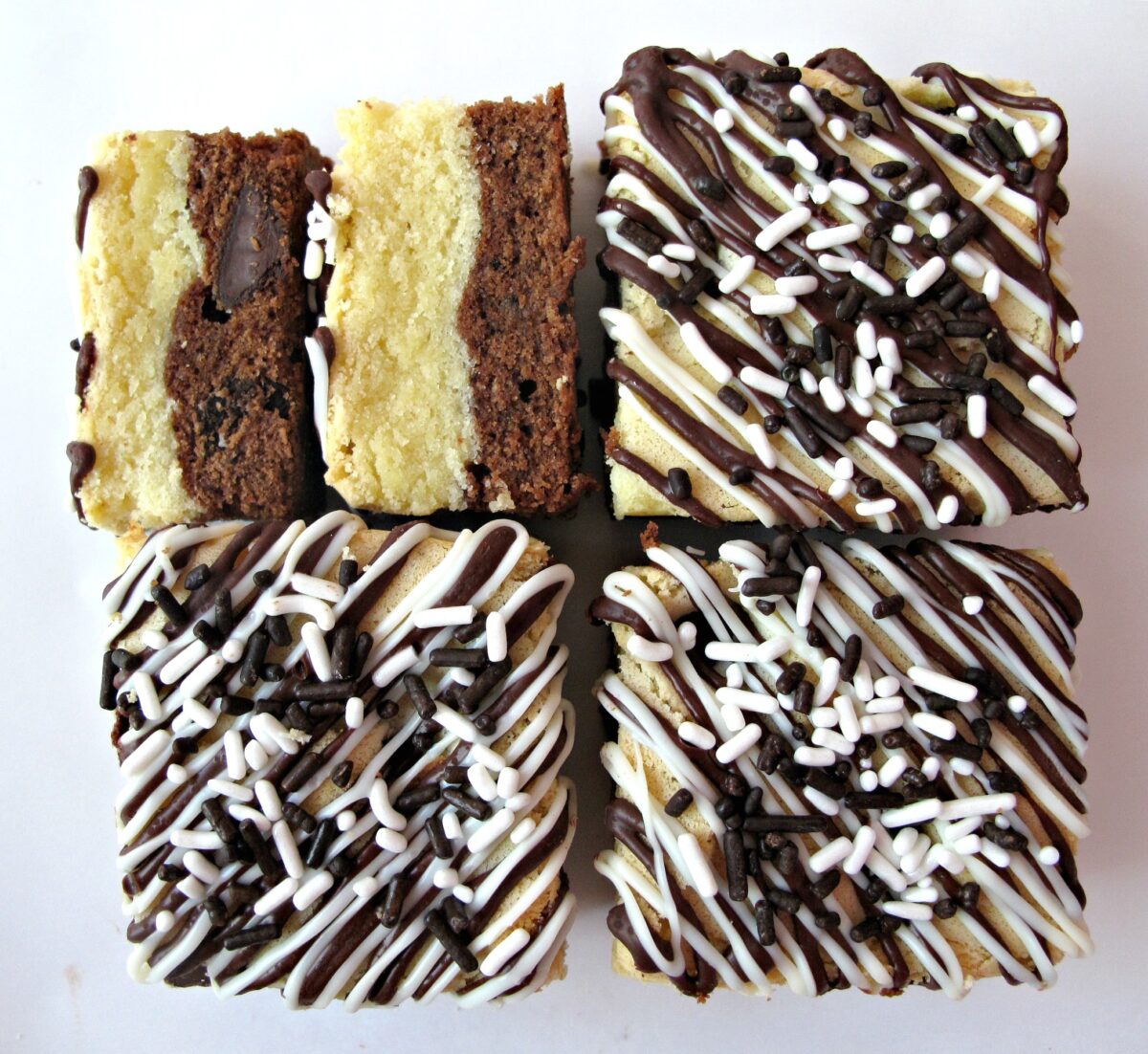 Four squares of Black and White bars decorated with melted chocolate zigzags and sprinkles.